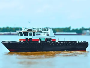 A black and red workboat from the Original Fleet, with large tires along the side, floats on a river with a blurred shoreline in the background.